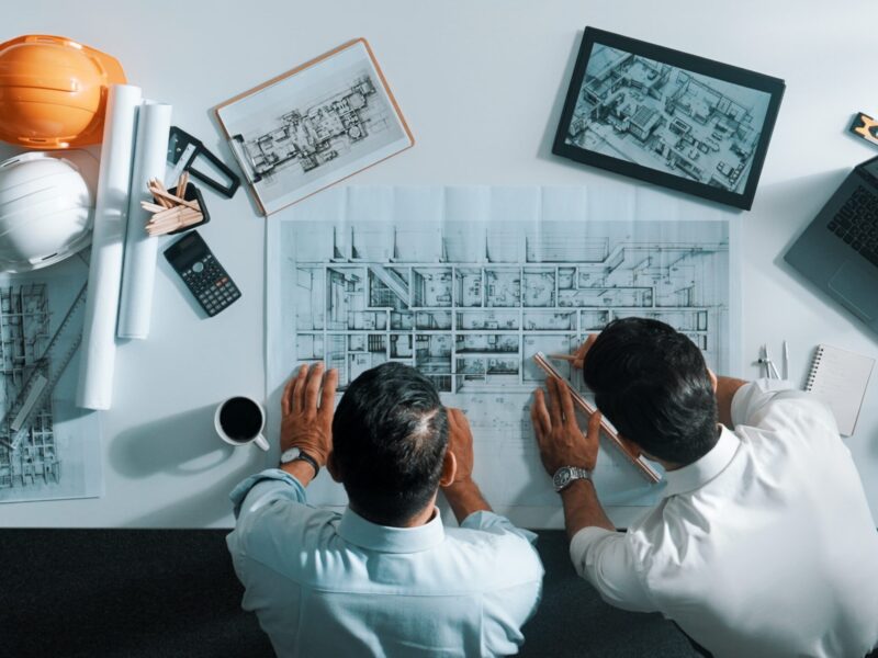 Top view of engineer working together to plan building design. Alimentation. Top view of skilled civil engineer working together to plan building design. Top down aerial view of skilled architect team sitting at table while manager using tablet open project plan. Alimentation.